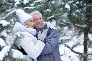 An elderly couple smiles in a snowy park. Aura Dental Center is committed to helping you and your smile look and feel their best.